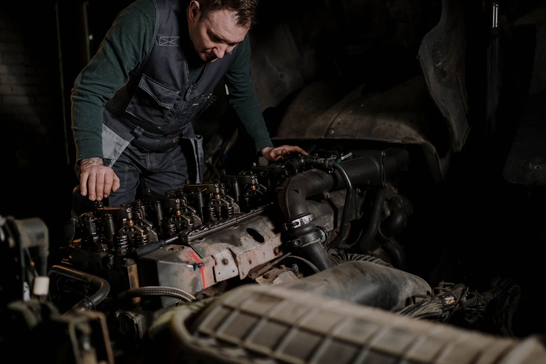 Mechanic in work vest inspecting engine block in dark workshop